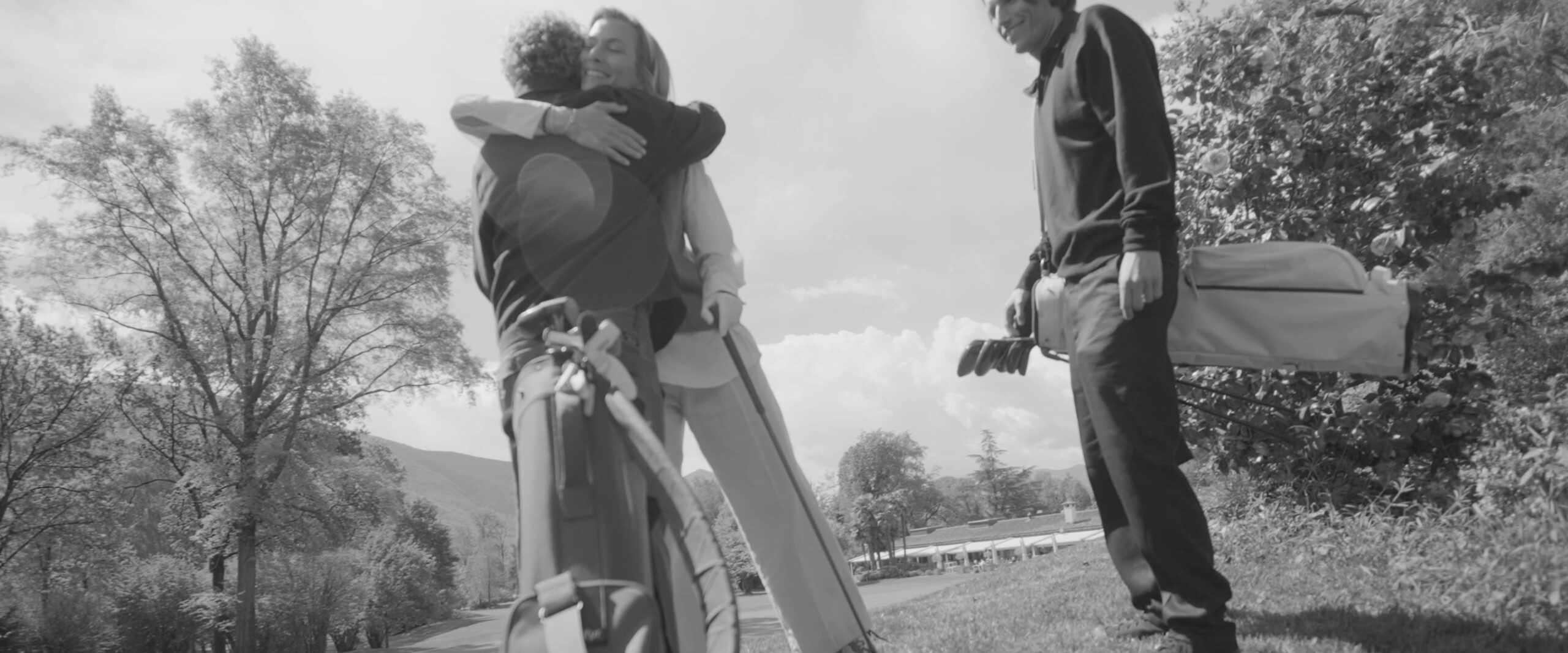 Olivier Widrig hugs a golfer after hitting a good shot, and Michael Noser stands nearby with his golf bag on his shoulder