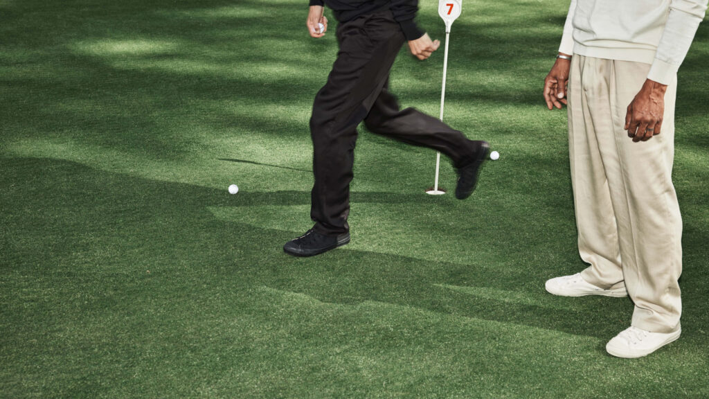 Two golfers on the green – one standing, one walking