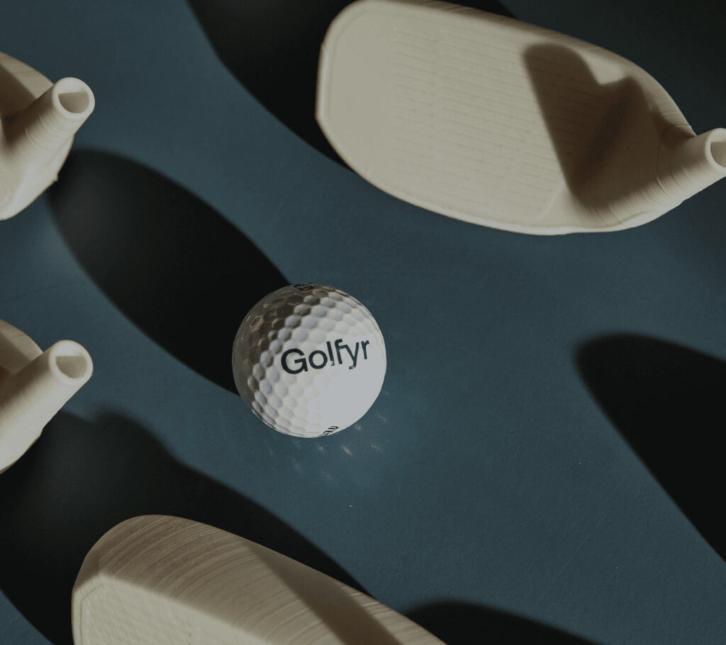 A Golfyr-branded golf ball on a desk near prototypes of different golf clubs