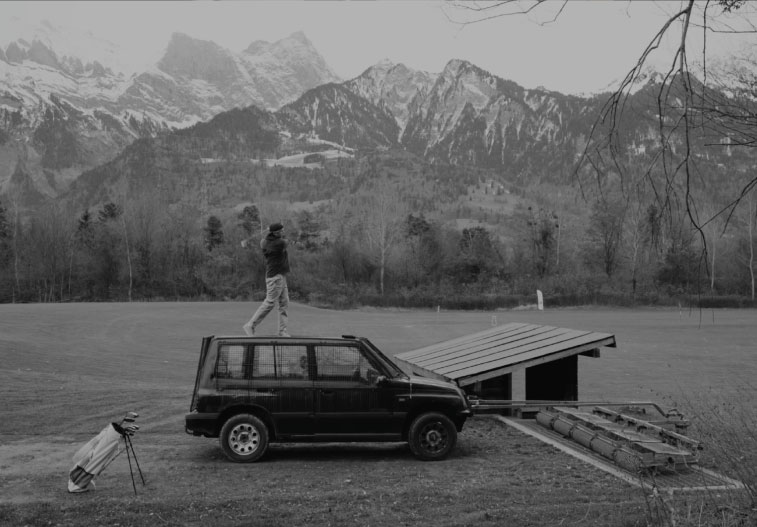 Olivier Widrig stands on a car and hits the tee
